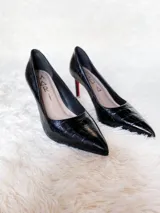 Zapatos de tacón alto con textura de reptil, color negro, con suela roja característica.