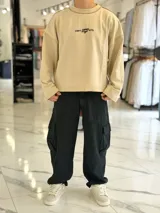 Buzo oversize color beige, con costuras externas visibles y gran estampado tipográfico y gráfico en la espalda.