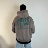 Canguro gris topo con capucha, corte boxy oversize y estampado en la espalda con la inscripción "MDW STUDIO" en verde agua.