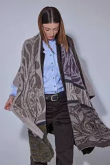 Ruana tejida en lana lambswool con diseño de bloques de color y tramas geométricas. Presenta cierre frontal con doble cursor y tiradores de cuero, permitiendo diferentes formas de uso.