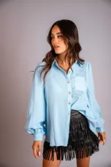 Camisa celeste de muselina con bordado floral en el hombro y bolsillo. Tiene corte holgado, cuello clásico, cierre con botones y mangas largas abullonadas.