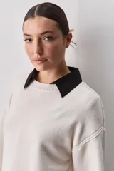 Sweater negro de tejido suave con escote redondo, mangas largas y calce relajado, con terminaciones acanaladas en cuello, puños y ruedo.
