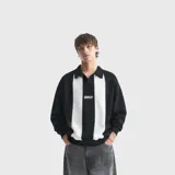 Buzo tipo polo de algodón, con diseño de bloques de color negro y blanco, cuello camisero y logo estampado en el pecho.