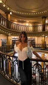 Corset blanco estilo off-shoulder, con escote en V pronunciado, volados de encaje en los hombros y cierre frontal con cordones ajustables.