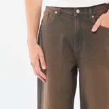 Pantalón de jean con corte baggy y pierna ancha, con efecto de lavado vintage en tono marrón oscuro. Cuenta con diseño clásico de cinco bolsillos, cierre frontal con botón y trabillas para cinturón.