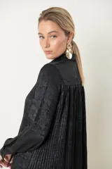 Camisa plateada de poliéster con textura metalizada, corte amplio, cuello clásico, cierre frontal con botones y mangas largas con puños abotonados.