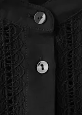 Blusa Lucy de diseño recto color negro, confeccionada en mezcla de algodón y viscosa. Cuenta con cuello mao, detalles bordados calados, manga larga y cierre frontal con botones.