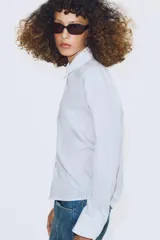 Camisa de algodón con estampado de rayas verticales, cuello solapa y puños en color blanco a contraste. Presenta cierre frontal con botones, bolsillo de plastrón en el delantero y bajo asimétrico.