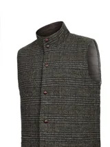 Chaleco de hombre con cuello alto, confeccionado en auténtica lana Harris Tweed con diseño de tartán en tonos marrones y grises. Presenta cierre frontal con botones, interior con relleno térmico y etiqueta distintiva de la marca en el ruedo.