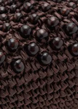 Bolso tipo clutch de tamaño pequeño, color marrón, elaborado en tejido de fibra natural con abalorios de madera incrustados y cierre a presión.