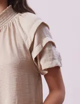 Blusa color beige de gasa con cuello fruncido, escote en V con lazo y mangas cortas con volados.