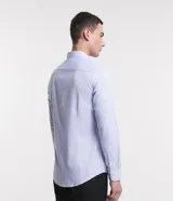 Camisa de manga larga con cuello inglés y cierre frontal abotonado. Confeccionada en tejido tricolina maquinetado con patrón de rayas finas, destacando por su alta transpirabilidad y suavidad.