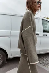 Jersey de punto con cuello subido y manga larga, de corte holgado. Presenta detalles de vivos en color crema en el cuello, puños y costuras de las mangas, contrastando con el tono marrón jaspeado de la prenda.