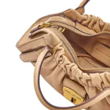 Cartera satchel compacta de cuero de cordero negro, con diseño estructurado, frunces en la parte superior, doble asa de mano y correa ajustable para llevar al hombro o cruzada. Incluye cierre metálico frontal con logo grabado.