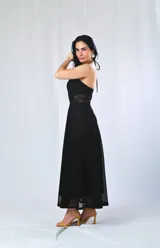 Vestido largo negro con escote halter y textura calada. Presenta un corte en la cintura con transparencia y un ruedo con detalle calado que deja ver la pierna.