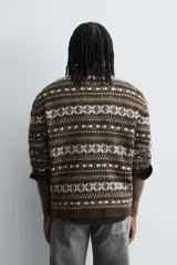 Jersey de punto con diseño jacquard geométrico en tonos marrones, blancos y azules. Presenta cuello redondo, manga larga y terminaciones en rib.