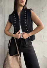 Chaleco negro de denim estilo militar, con doble botonadura metálica frontal, cuello alto y detalles deshilachados en las sisas.