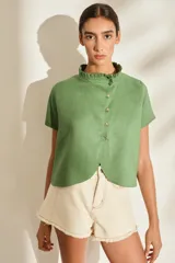 Blusa de lino verde de manga corta y corte recto, con cuello alto con volado y cierre frontal cruzado con botoncitos dorados.