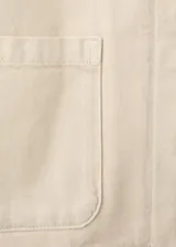Chaqueta de algodón estilo tejano en color beige, con cuello camisero, manga larga, dos bolsillos de parche en el frente y cierre delantero de botones.