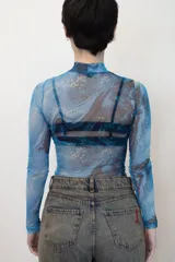 Remera traslúcida de cuello alto y mangas largas, con estampado abstracto en tonos celeste, azul y amarillo.