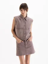 Chaleco de denim color marrón, con cuello camisero, cierre frontal con broches metálicos y bolsillos delanteros parcheados.