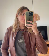 Colgante con dije de bronce con forma de coral y cordón de cuero marrón.