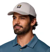 Gorra Columbia Twin Canyon Ball Cap color gris, con visera curva, ojales bordados para ventilación y un parche frontal cuadrado con el logo de la marca en negro, amarillo, marrón y blanco.
