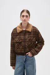Campera corta de estilo bomber con estampado a cuadros en tonos marrones. Presenta cuello de corderito sintético, cierre frontal con cremallera, dos bolsillos frontales con solapa y puños y ruedo de tejido elástico acanalado.