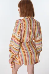 Minifalda estampada con motivos geométricos en tonos amarillo, naranja, celeste y rosa. Tiene corte evasé y lazo para ajustar en la cintura.