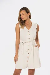 Vestido corto sin mangas color beige claro, con escote en V, botones frontales de madera y cinturón de lazo a juego. Presenta pequeños volados en los hombros y bolsillos laterales.