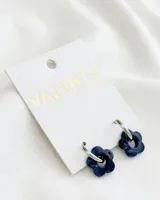 Aros de acero plateado con dije colgante de acrílico azul en forma de flor.