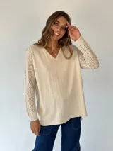 Buzo de punto color beige con escote en V, mangas largas con textura calada y cuerpo de tejido liso.
