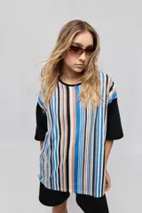 Remera oversize de manga corta con diseño de rayas verticales en tonos rojos, negros, blancos y tostados, y mangas blancas lisas.