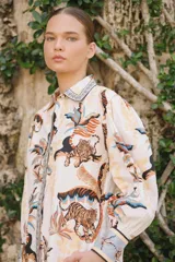 Camisa de popelina de algodón blanca con estampado tropical de tigres y palmeras en tonos neutros y azules, cuello camisero, mangas largas abullonadas con puños anchos y botonadura frontal oculta.