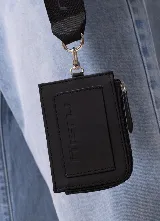 Billetera Rusty modelo Runoi de color negro, con cierre de cremallera y correa de muñeca de tela con el logo de la marca estampado en repetición. Incluye mosquetón metálico plateado para enganchar la correa.