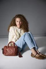 Bolso de mano tipo doctor bag o bowling bag, color marrón cuero, con diseño acolchado en rombos y tachas doradas. Posee doble asa de mano y un dije colgante de flecos largos de cuero marrón.