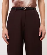 Pantalón de sastrería negro de corte recto, confeccionado en crepé, con cintura con pasadores, cierre frontal y un cinturón fino con hebilla metálica.