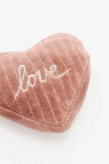 Monedero en forma de corazón confeccionado en terciopelo color verde esmeralda, con costuras verticales acolchadas y la palabra 'love' bordada en hilo dorado. Incluye un cierre con tirador de borla a tono.