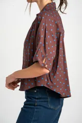 Blusa color crudo con estampado de lunares marrones, cuello camisero, cierre frontal con botones y mangas cortas holgadas.