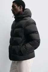 Campera puffer negra con capucha ajustable con elásticos, cuello alto, cierre frontal con cremallera, bolsillos laterales y puños elásticos ajustables.