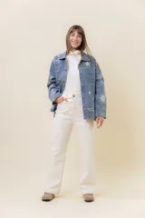 Camisa de denim de lavado medio, con calce relajado y ligeramente oversize. Presenta bordados o estampados de inspiración celestial (soles, lunas y estrellas) en color claro en la parte delantera y mangas. Tiene cuello, bolsillos delanteros con tapa y cierre frontal con botones.