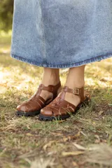 Sandalias tipo pescador confeccionadas en cuero vacuno color marrón, con diseño de tiras entrelazadas, tira en T, hebilla de ajuste en el tobillo y suela track robusta.