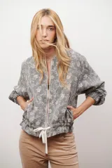 Bomber de tela liviana color beige con textura sutil, cierre frontal completo, mangas largas con puños elásticos y cordón ajustable en el ruedo.