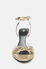 Sandalia de tacón alto fino color dorado con efecto metalizado, tiras delanteras cruzadas con detalle de nudo y cierre de hebilla en la pulsera del tobillo.