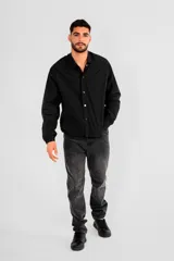 Campera negra de poliéster con cuello camisero, cierre con botones a presión, mangas largas con puños elásticos y bolsillos laterales.