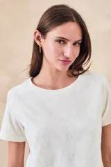 Remera de algodón color blanco con bordados florales y geométricos en color negro. Presenta cuello redondo, mangas cortas y un diseño con franjas horizontales bordadas.