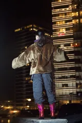 Abrigo corto de piel sintética color marrón, con cuello alto y bolsillos colgantes sujetos con cadenas.