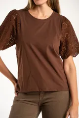 Remera de algodón peinado color negro, con mangas cortas de broderie con diseño calado y terminación festoneada. Presenta un corte oversize y cuello redondo.