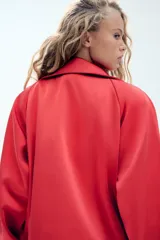 Cazadora roja de satén con cuello subido, manga larga con hombreras, bolsillos delanteros con cierre, bajo ajustable con cordón elástico y cierre frontal de cremallera metálica.