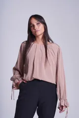 Blusa de manga larga color rosado, con cuello redondo y puños elásticos con volados y lazos decorativos. Presenta un diseño holgado con frunces en el escote.